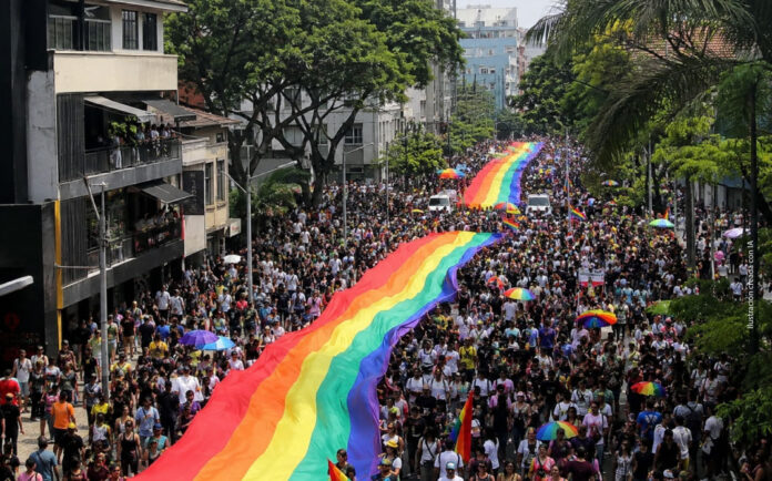 Multitud participa en la Marcha del Orgullo en Medellín portando una gran bandera arcoíris mientras una editorial reflexiona sobre diversidad, pluralismo y libertad de conciencia.