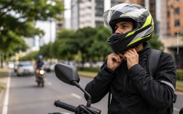 Motociclista utilizando correctamente un casco certificado y ajustando la correa de seguridad antes de conducir por una vía urbana.