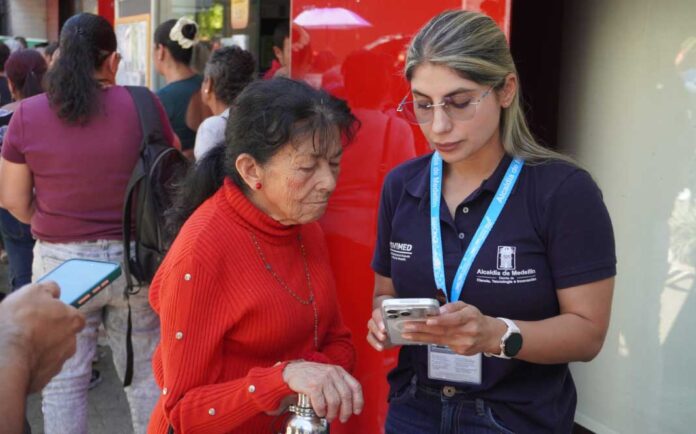Una funcionaria de la Alcaldía de Medellín acompaña a una mujer mayor durante la votación de Presupuesto Participativo.